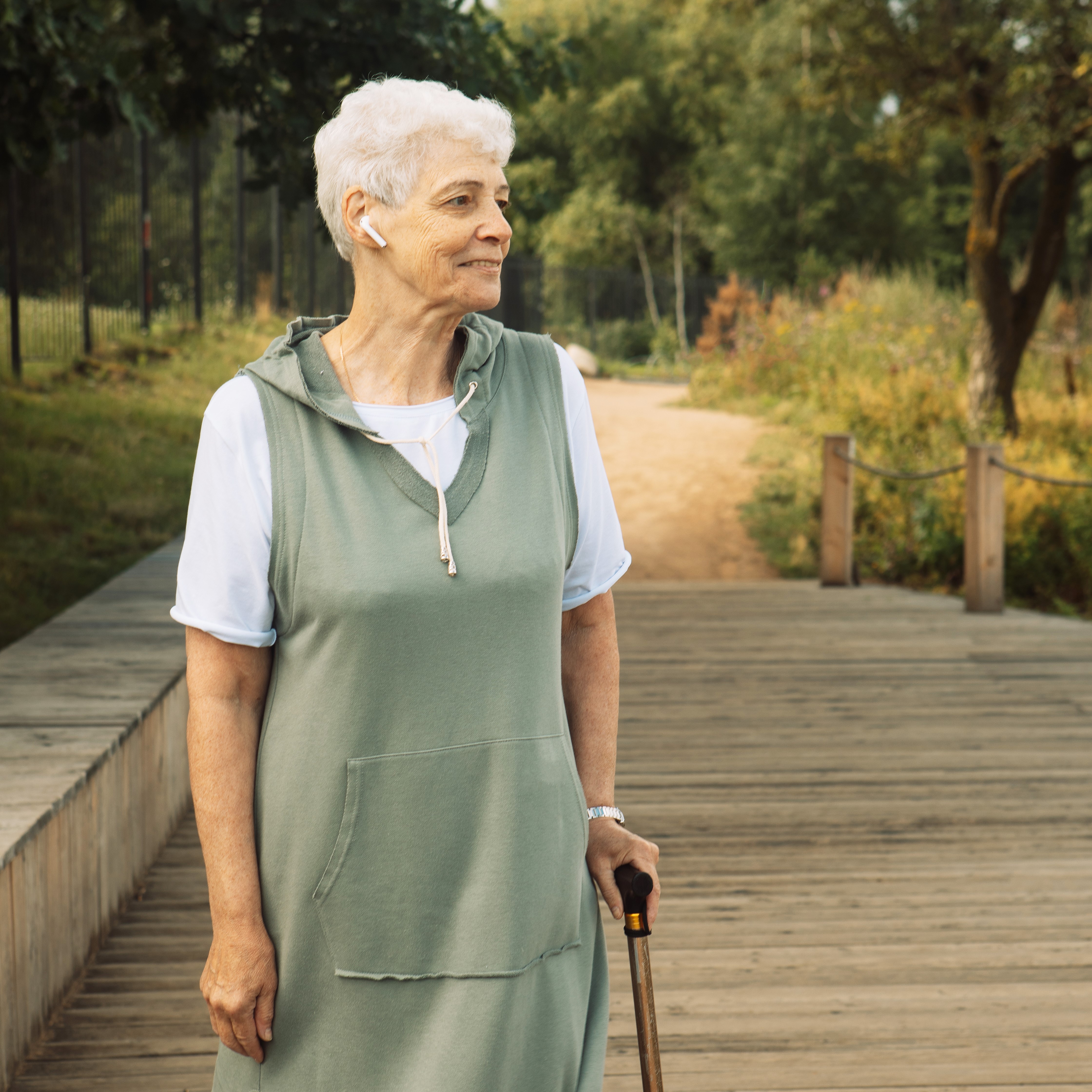 Older woman using earbuds and a cane pauses along a path
